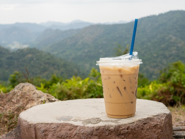 A glass of iced coffee is placed on a rock against a background of mountains and sky