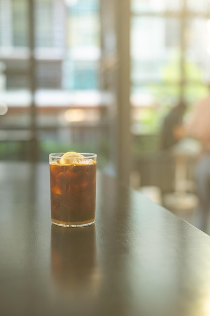 A glass of iced coffee with ice on a table in front of a window.