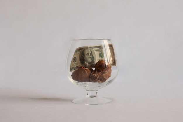 A glass is on the table In the buck are shells and a dollar bill