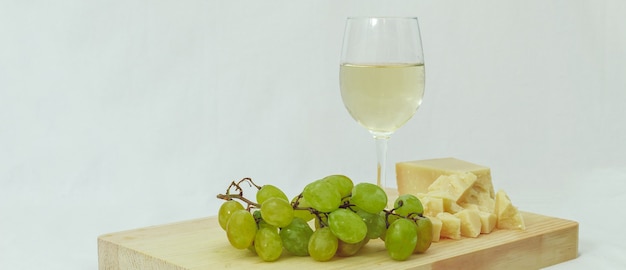 A glass of Italian white wine served with parmesan and grapes on a wooden cutting board with a white background