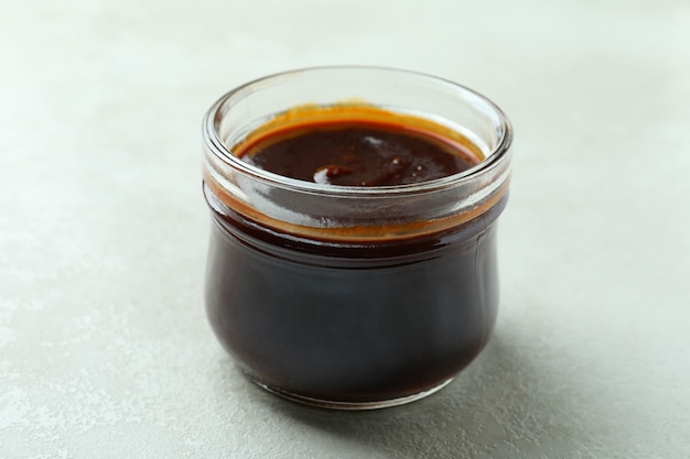 Glass jar of barbecue sauce on white textured