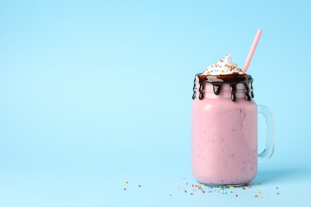 Glass jar of delicious berry milkshake on blue background