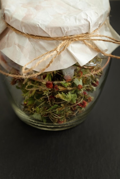 Glass jar filled with dried wild strawberries closed with piece of craft paper and tied with twine