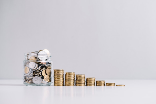 Glass jar full of money in front of decreasing stacked coins