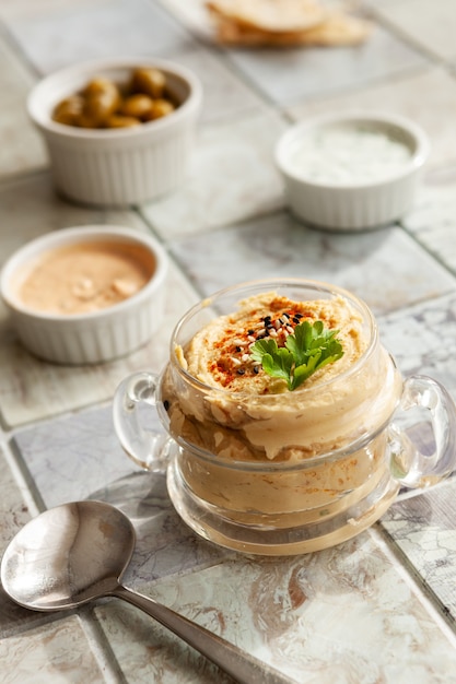 Glass jar of hummus, traditional Jewish, Arabian, Middle Eastern food from chick-peas with deeps and with pita flatbread on ceramic tile background. Close up, selective focus