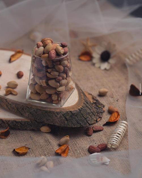 A glass jar of nuts sits on a piece of wood with other nuts on it