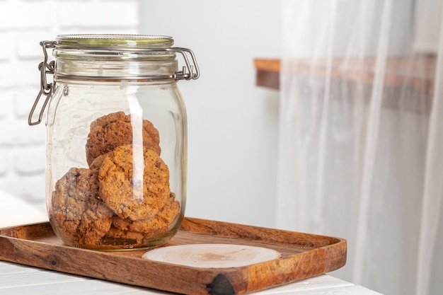 Glass jar of oat cookies on wooden tray in kitchen