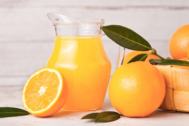 Glass jar of organic fresh orange juice with raw oranges on light wooden background