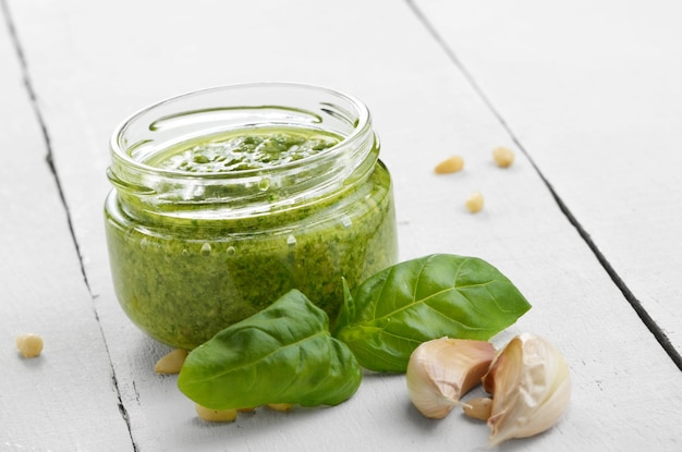 Glass jar of pesto sauce on white kitchen table closeup