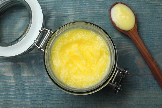 Glass jar and spoon of Ghee butter on light blue wooden table flat lay