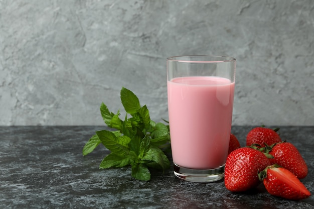 Glass jar of strawberry milkshake and ingredients on black smokey table