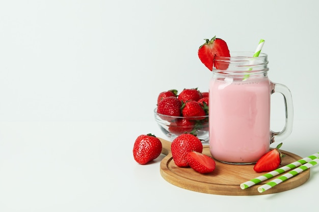 Glass jar of strawberry milkshake and ingredients on white table