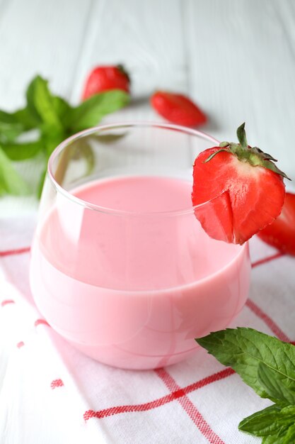 Glass jar of strawberry milkshake and ingredients on white wooden table