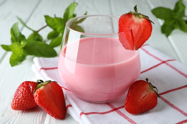 Glass jar of strawberry milkshake and ingredients on white wooden table