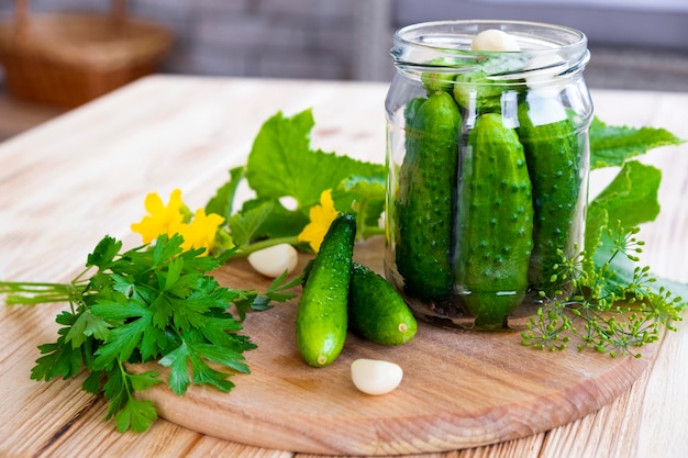 Glass jar with fresh cucumbers herbs garlic dill and parsley on wooden board Cooking pickle cucumbers for home conservation