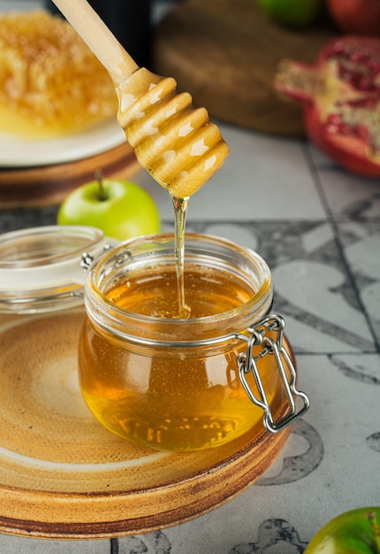 Glass jar with fresh honey honey spoon apple and pomegranate concept jewish new year happy holiday