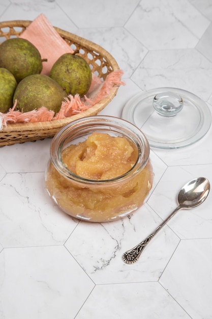 Glass jar with mashed pears and fresh pears in a wicker plate on a light background Vertical orientation