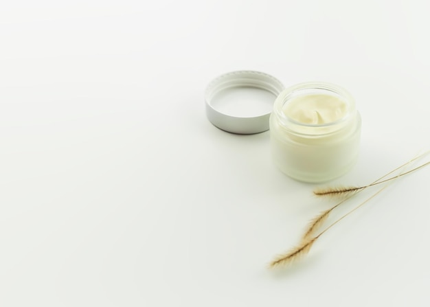 glass jar with moisturizing cosmetic cream and decorative dry grass on a white table