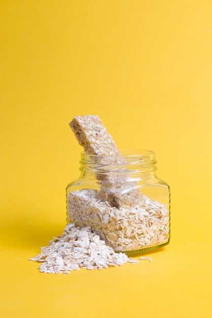 Glass jar with oatmeal and several protein bars for a snack on a yellow surface