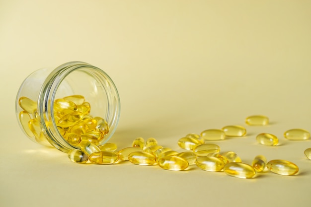 Glass jar with omega 3 fish fat oil capsules on yellow background.