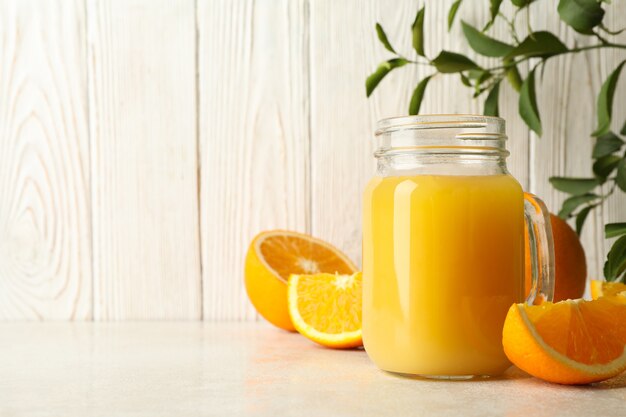 Glass jar with orange juice against white wooden