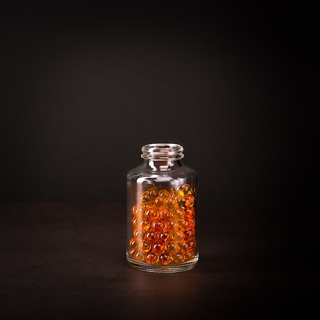 A glass jar with orange pills on dark background