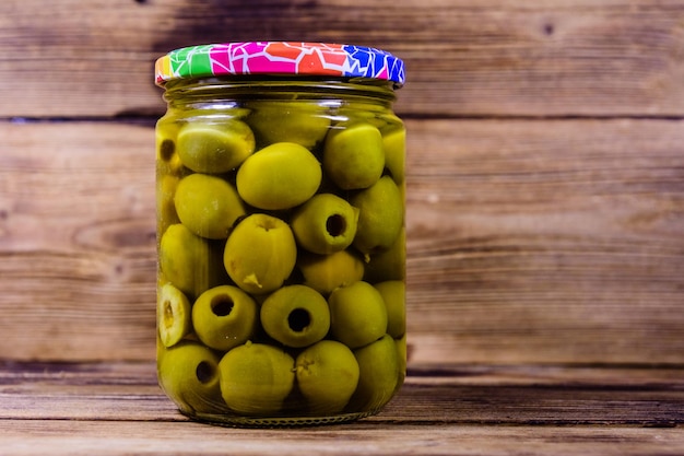 Glass jar with pickled green olives on wooden table