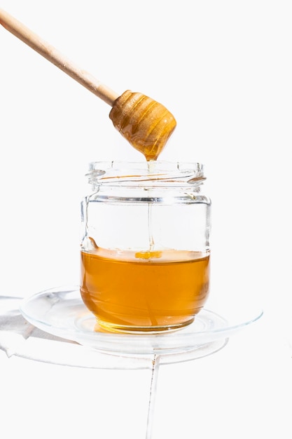 Glass jar with raw flower honey and wooden honey taster stick