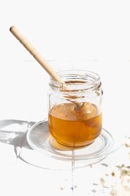 Glass jar with raw flower honey and wooden honey taster stick