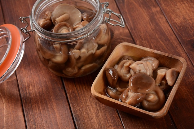 Glass jar and wooden bowl with homemade pickled forest mushrooms honey agarics on old wooden board Fermented healthy food