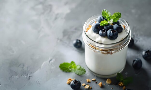 Photo glass jar of yogurt topped with nutritious granola and fresh blueberries