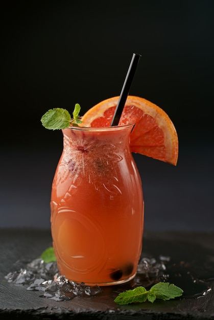 Glass jars with fresh grapefruit juice and ripe grapefruits on black background