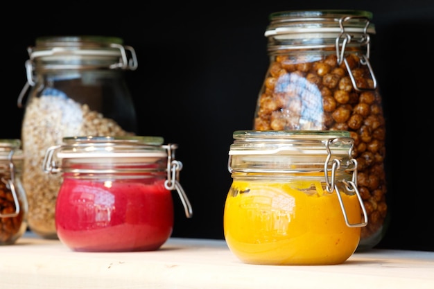 Glass jars with grain nuts butter jam on the wooden shelf on background of a dark wall breakfast concept kitchen background healthy eating concept conservation concept