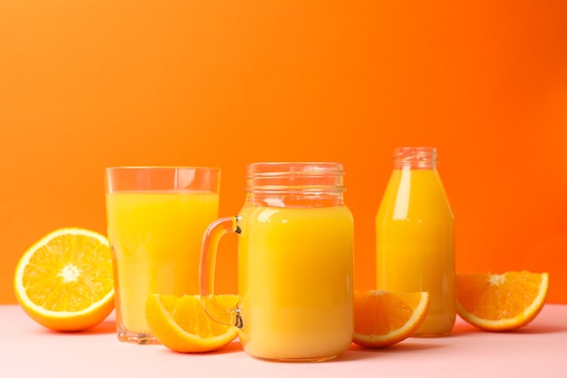 Glass jars with orange juice on pink table