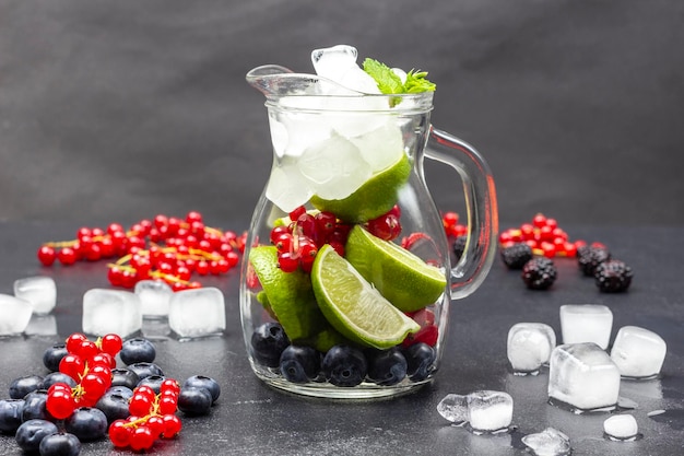 Glass jug with berries ice and lime Sprigs of red currant ice and blueberry on table