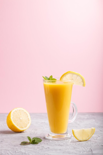 Glass of lemon drink on a gray and pink background. Morninig, spring, healthy drink concept. Side view,  copy space.