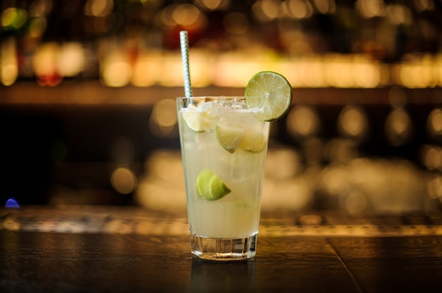 Glass of a Lemonade cocktail decorated with lime and ice cubes on the wooden steel bar counter