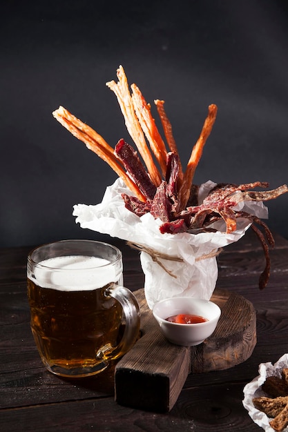 Glass of light beer and snacks on wooden dark table