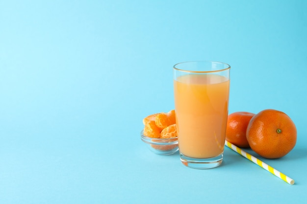 Glass of mandarin juice, straw and ingredients on blue background