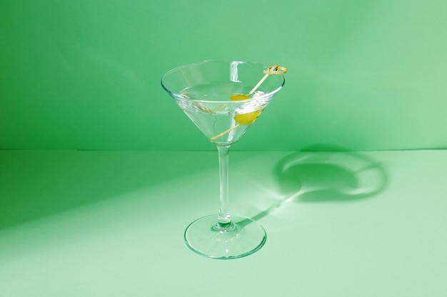 Glass of martini cocktail with green olives. Focus on shadows