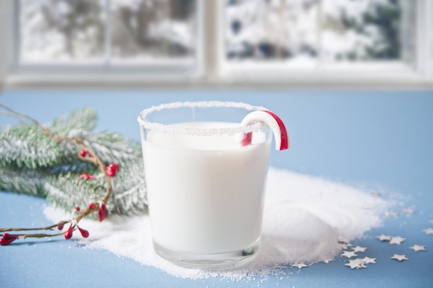 Glass of milk, candy cane, christmas pine branch on the blue  nearby frozen winter window