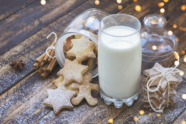 Glass of milk and cookies on brown wooden table with christmas lights