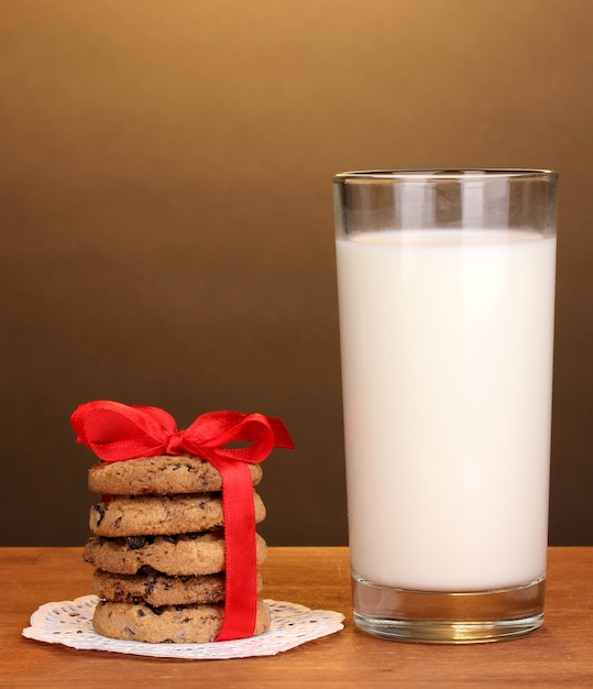 Glass of milk and cookies on wooden table on brown background