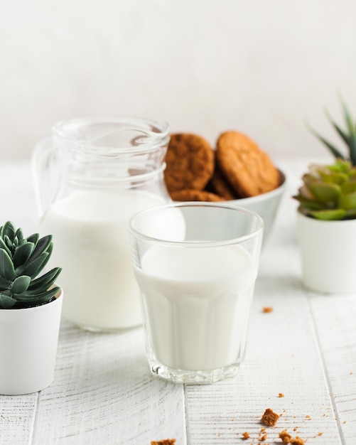 A glass of milk, a jug of milk, cookies on a light background