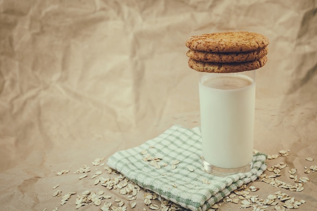 Glass of milk and oatmeal cookies on crumpled paper background