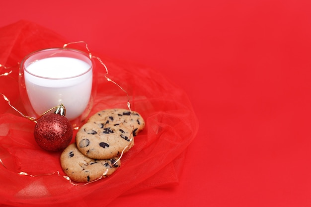 A glass of milk with cookies and a Christmas tree toy on a red background. New Year