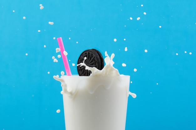 Glass of milk with a pink straw and a cookie splashing