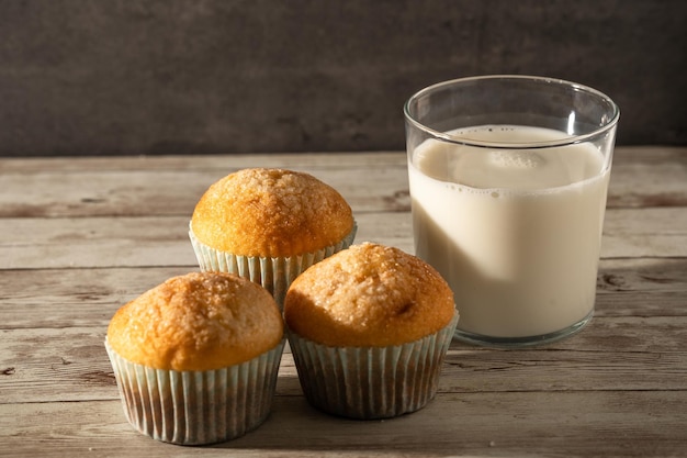 Glass of milk with three freshly baked muffins in the foreground breakfast snack pastries concept