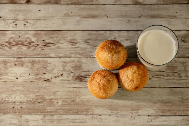 Glass of milk with three freshly baked muffins in the foreground breakfast snack pastries concept