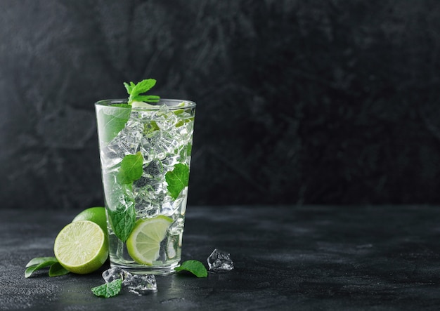 glass of mojito cocktail with ice cubes mint and lime on black background